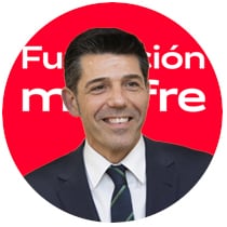 Retrato corporativo em formato circular de um homem sorridente com terno escuro, camisa branca e gravata azul marinho, em fundo vermelho com parte do logotipo da Fundación Mapfre em branco.