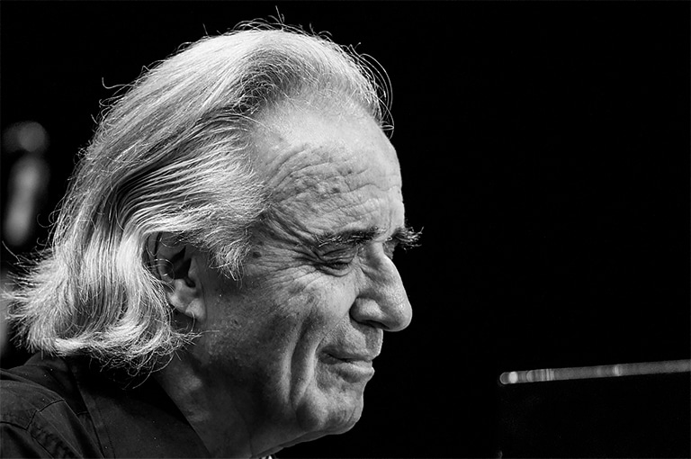 Maestro João Carlos Martins Retrato em preto e branco do Maestro João Carlos Martins, pianista clássico e maestro brasileiro, capturado em um momento de concentração e emoção enquanto toca piano. Seu rosto transmite serenidade e paixão pela música, com cabelos brancos e longos, e uma expressão profunda que revela sua dedicação e amor pela arte.