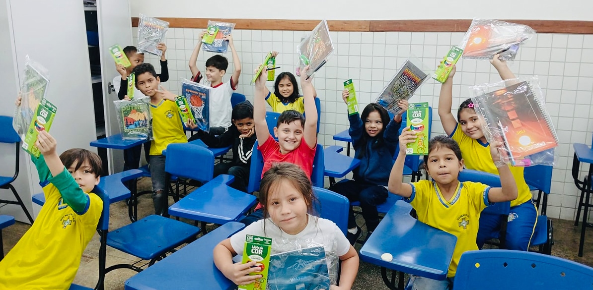 Alunos de projeto de reforço escolar em Manaus segurando cadernos e materiais escolares dentro de sala de aula durante atividade educativa da AEVA.