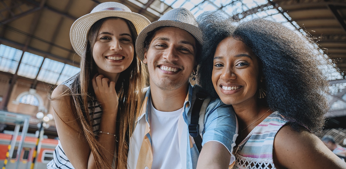 Dia Internacional da Felicidade Três jovens sorriem enquanto tiram uma selfie na plataforma de uma estação ferroviária.