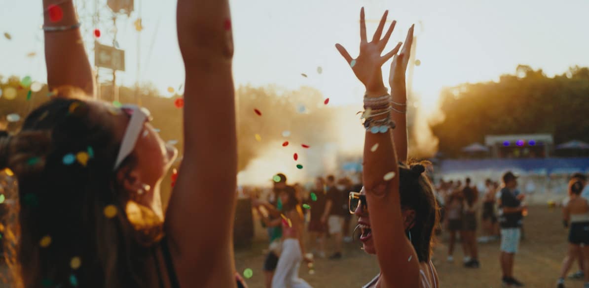 O poder silencioso da cultura Cena animada de um festival de música, com uma multidão vibrante celebrando sob o sol. Confetes coloridos flutuam no ar enquanto as pessoas levantam as mãos, imersas na atmosfera festiva. Este momento alegre simboliza o espírito do "Dia Nacional da Cultura", uma celebração da unidade cultural.