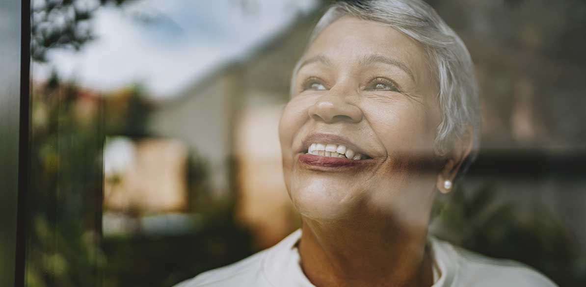 Mulher sorrindo junto à janela simbolizando esperança e novos caminhos.