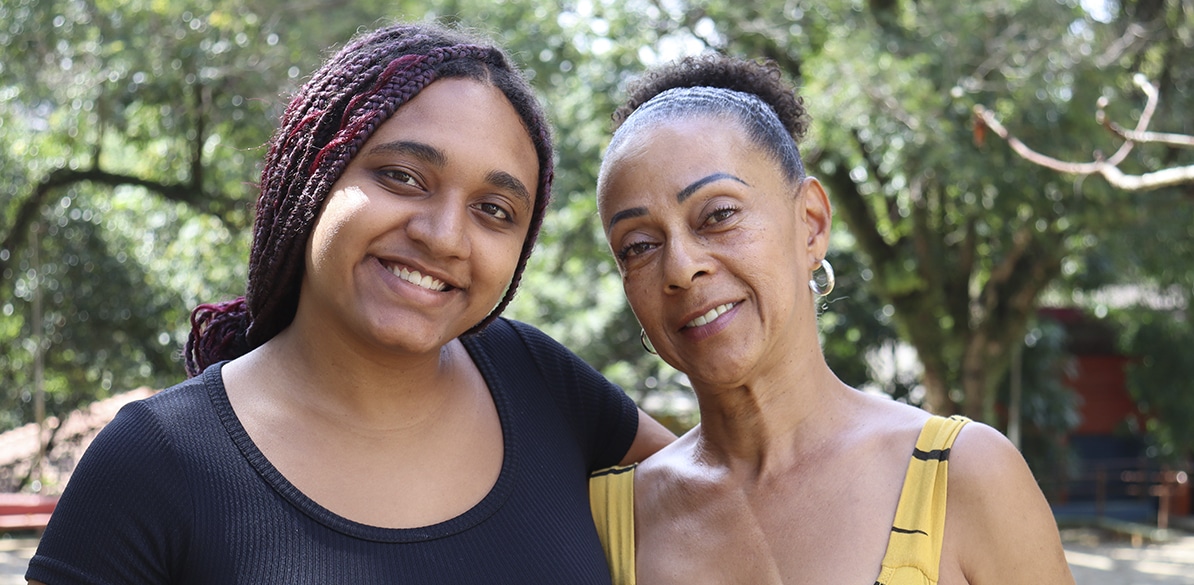 Mãe e filha sorrindo juntas ao ar livre cercadas pela natureza durante uma celebração em familia