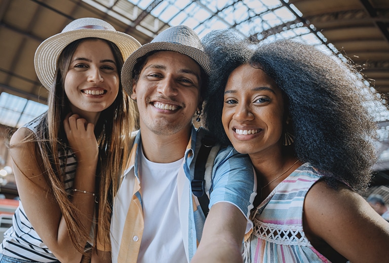 Dia Internacional da Felicidade Três jovens sorriem enquanto tiram uma selfie na plataforma de uma estação ferroviária.