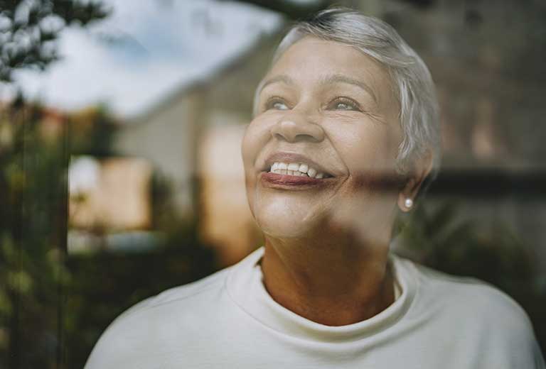 Dia Internacional da Esperança Mulher sorrindo junto à janela simbolizando esperança e novos caminhos.